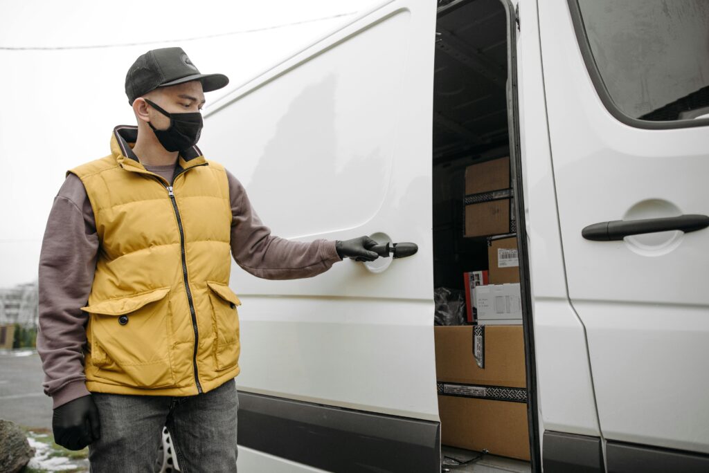 Delivery person opening a van full of packages, wearing a face mask and gloves.
